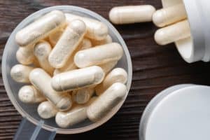 Weiße medizinische Kapseln von Glucosamin Chondroitin, gesunde Ergänzung Pillen in der Kunststoff-Löffel auf hölzernen Hintergrund, Makro-Bild, Ansicht von oben